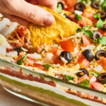 7 layer dip and a hand with a chip dipping in